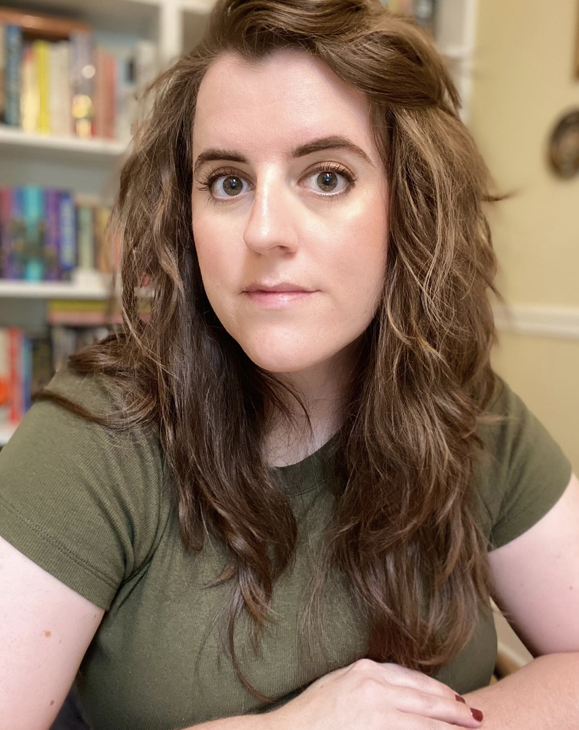 A photo of the author sitting in front of her bookshelves wearing an olive green shirt.